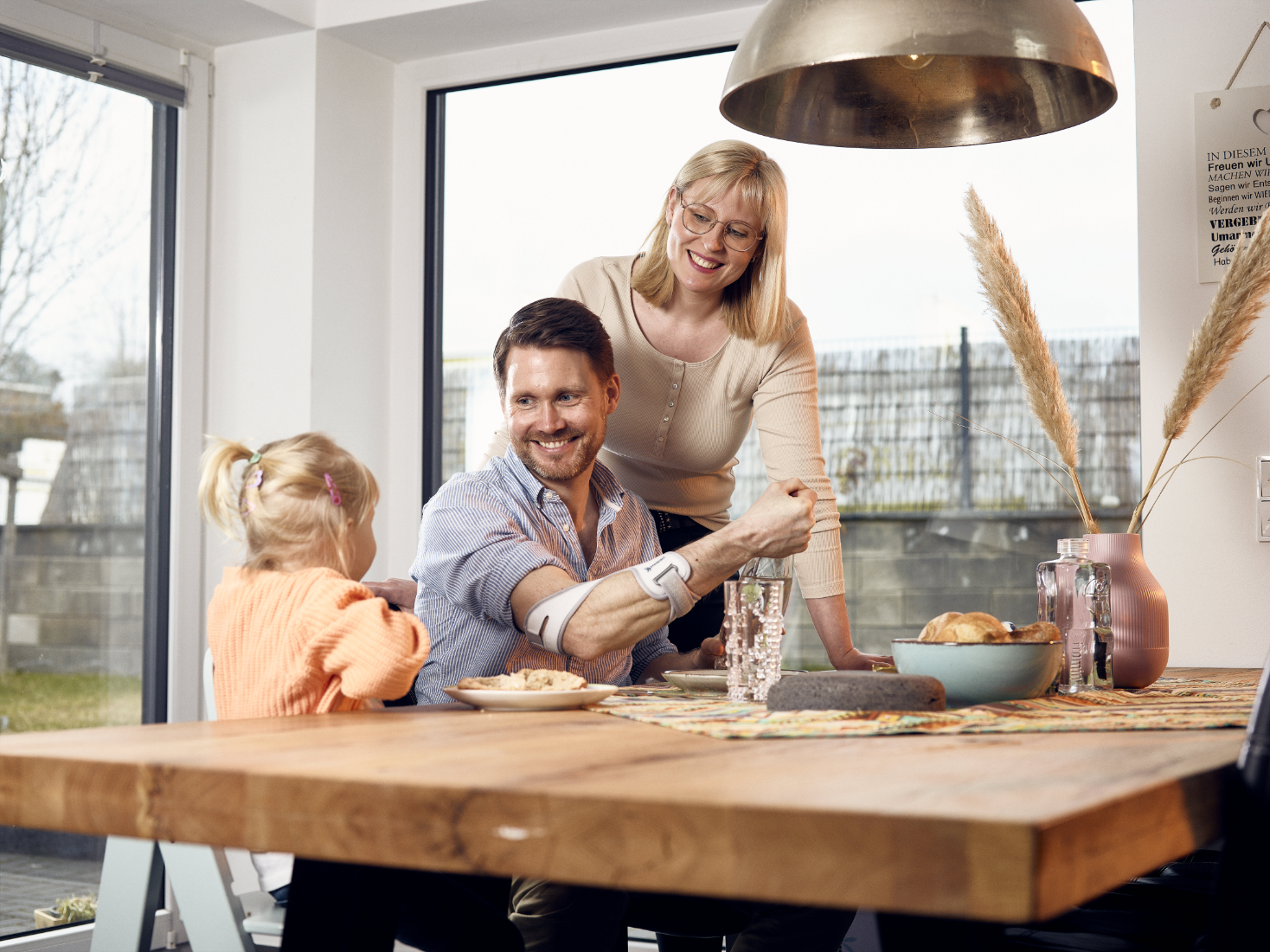 The Masalo Cuff - relieves pain and supports your arm in everyday life A father wearing the Masalo cuff is sitting at the breakfast table with his family and opens a water bottle