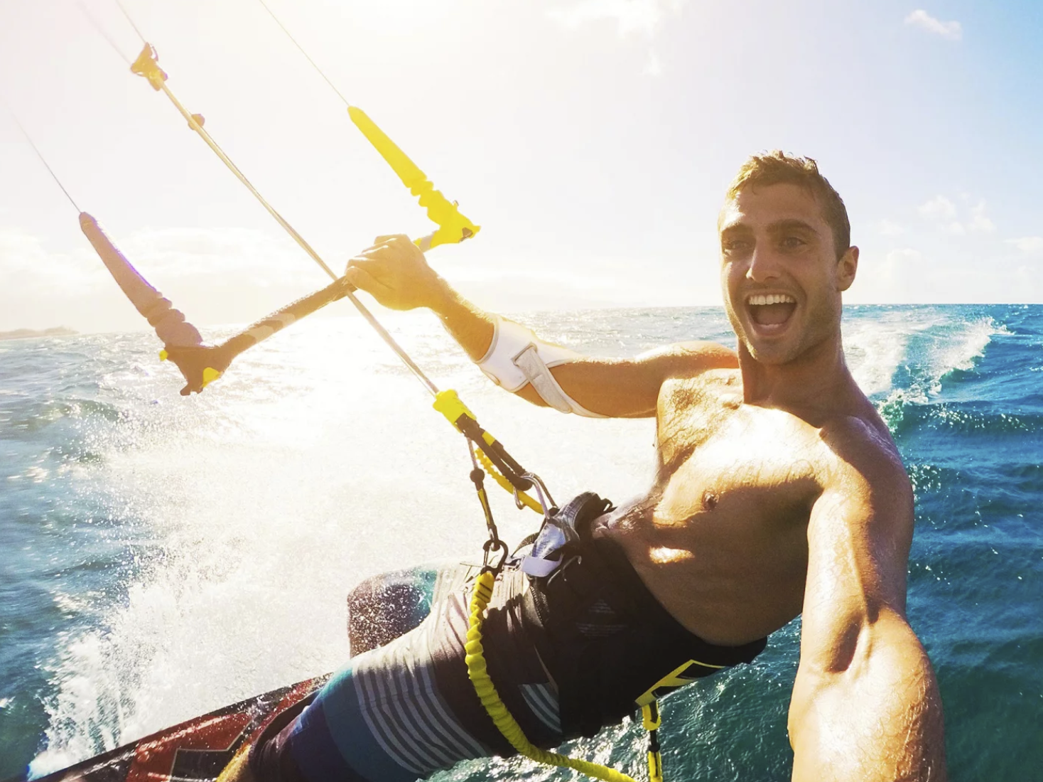 The Masalo Cuff – also suitable for water sports A young, athletic, laughing man wearing the Masalo cuff while kitesurfing in the ocean.